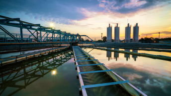Water at a treatment plant reflects the cloudy twilight sky with silos in the distance