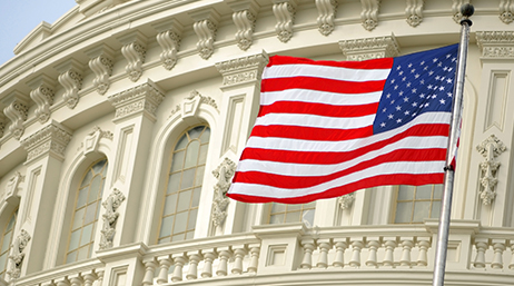 An American flag flying in front of the highly decorated ivory-colored façade of a government building 