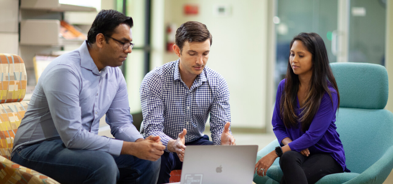Three businesspeople sitting in a working space looking at a laptop on the table in front of them