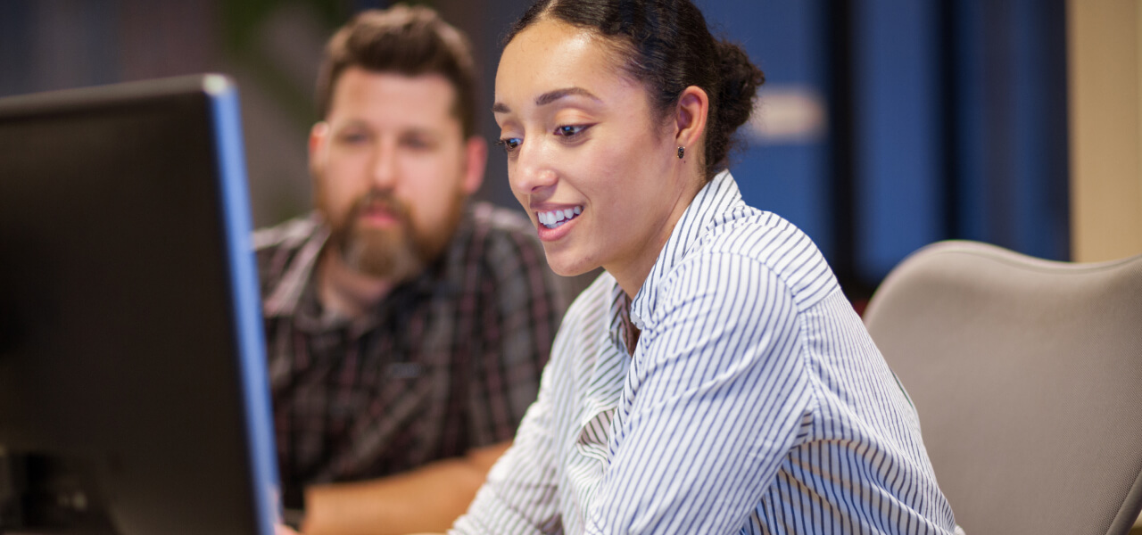 Three businesspeople sitting in a working space looking at a laptop on the table in front of them