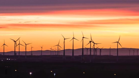 The horizon at sunset shows the silhouettes of a wind turbine farm against the sky.
