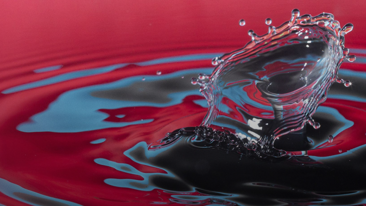 A splash of water creates ripples in a pool reflecting bright pink and blue colors. 
