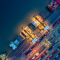 An aerial image of a loading dock filled with rows of brightly-colored cargo containers with a cargo ship waiting in the dark blue waters