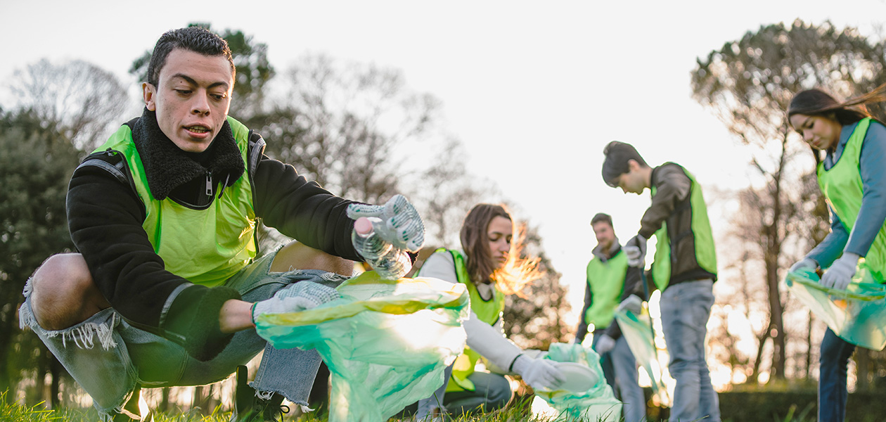 A group of volunteers in safety vests gather litter into trash bags in a sunny public park