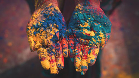 Rainbow colored paint on outstretched palms of hands