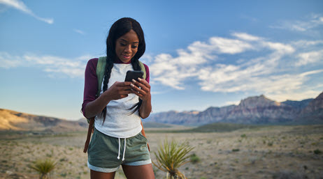 Young woman walking in a desert holding a mobile phone