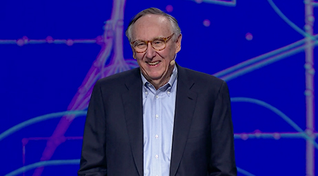 Esri President Jack Dangermond wearing business attire and a microphone and smiling overlaid with a play button