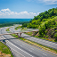 A five-lane highway curving through lush, green rolling hills on a sunny day 