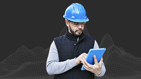 Personne portant un casque bleu et des lunettes de sécurité et travaillant sur une tablette, devant une représentation filaire d’une chaîne de montagnes