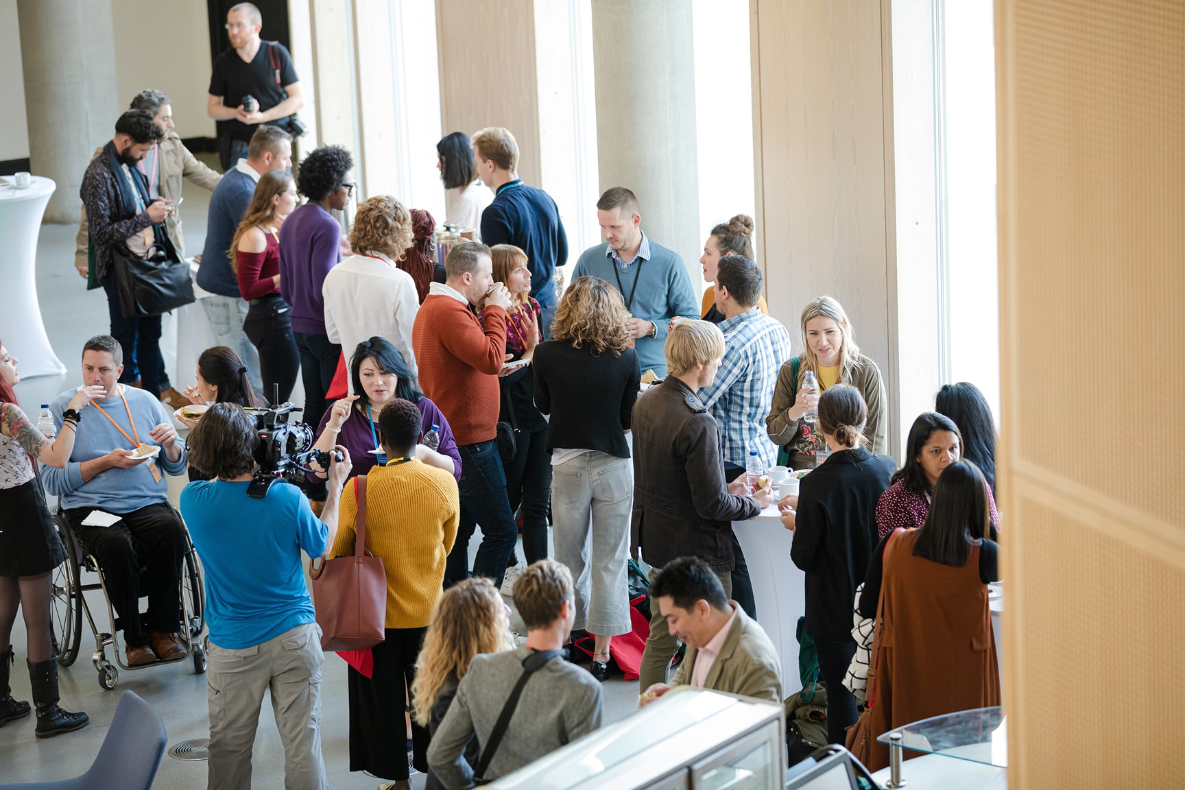A large group of people gathers in a bright indoor space during a conference or networking event