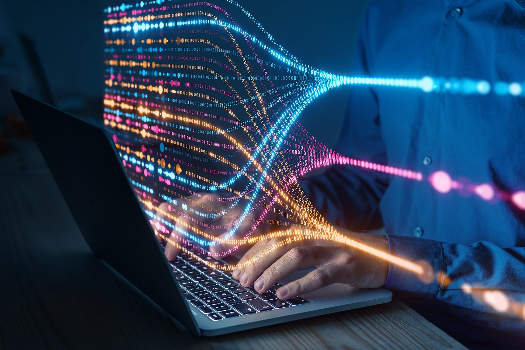 A person types on a laptop computer while colorful digital data streams flow outward from the keyboard