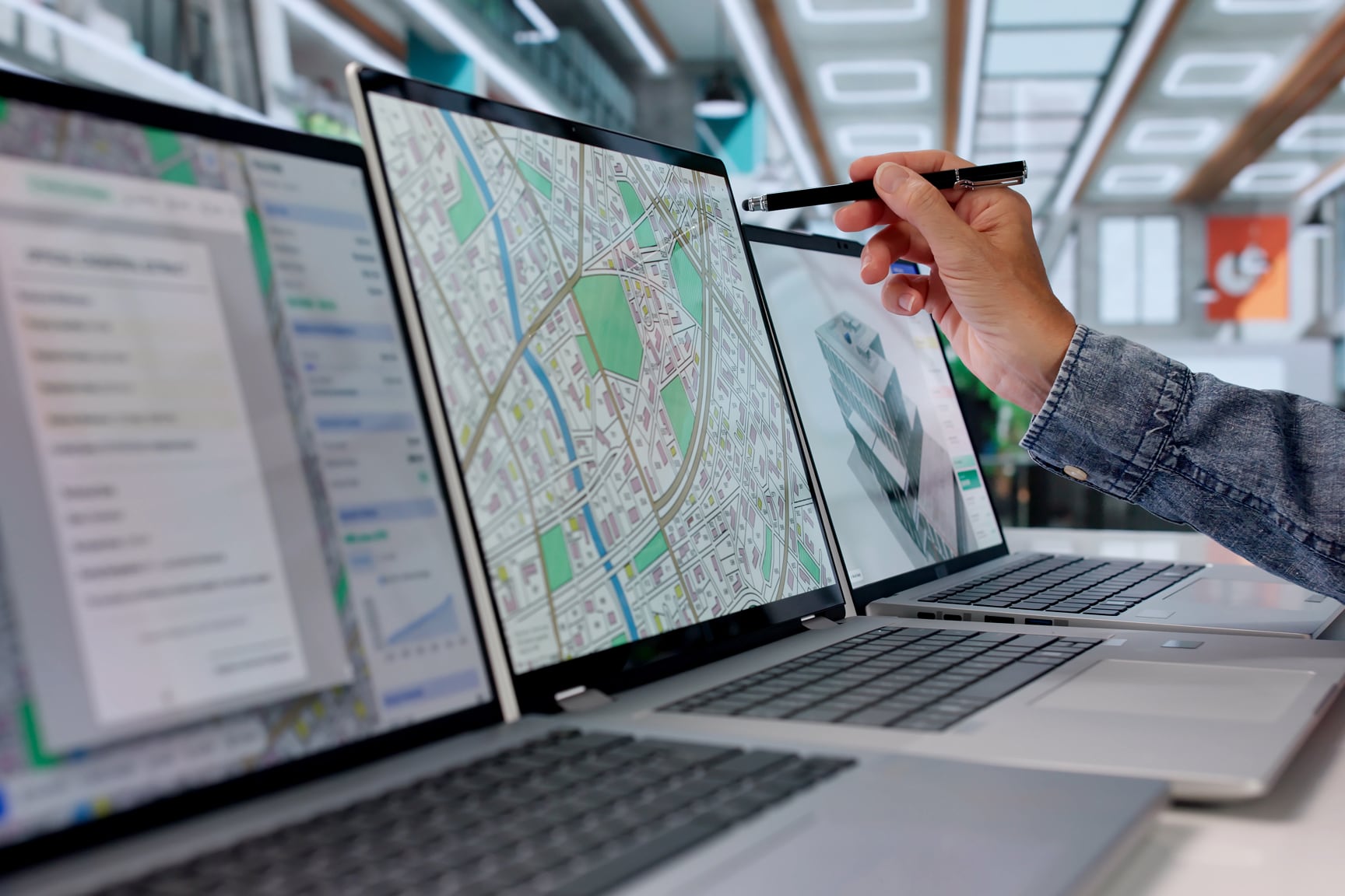 A person uses a stylus to point at a laptop screen displaying a detailed digital city map