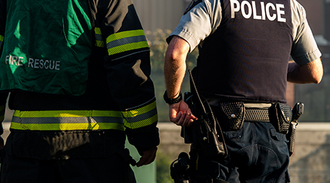 A police officer and a firefighter stand side by side, viewed from behind