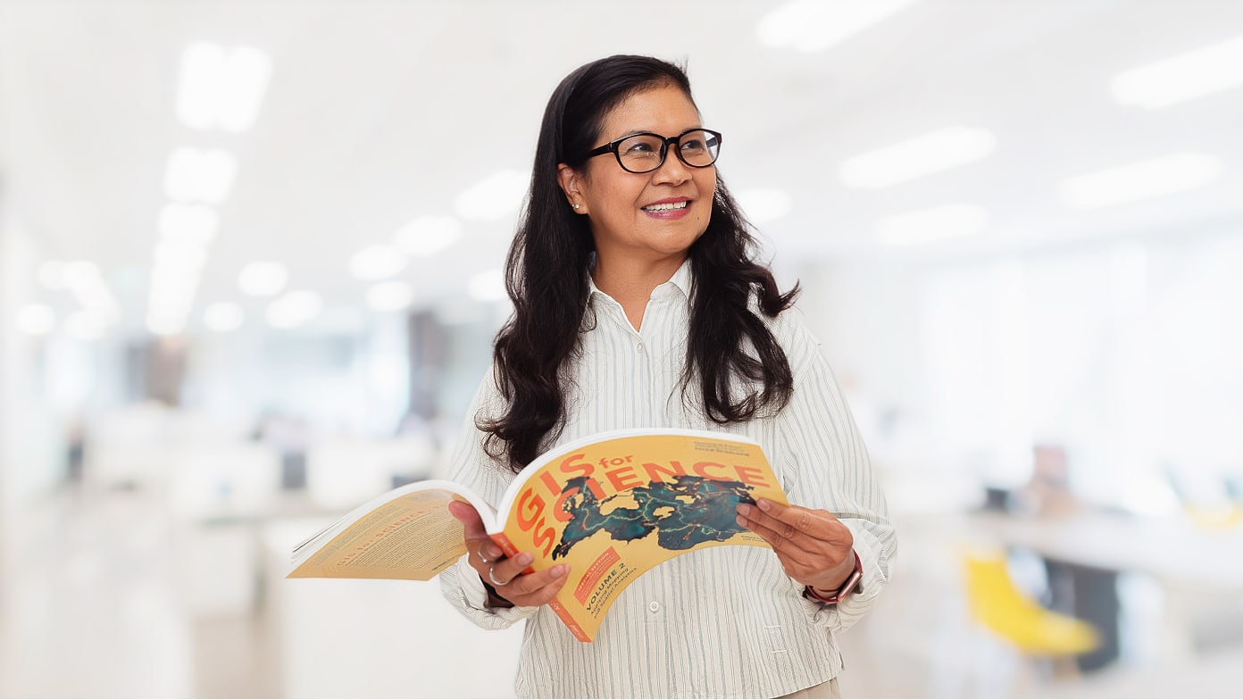 A woman stands in a modern, bright office holding an open magazine.