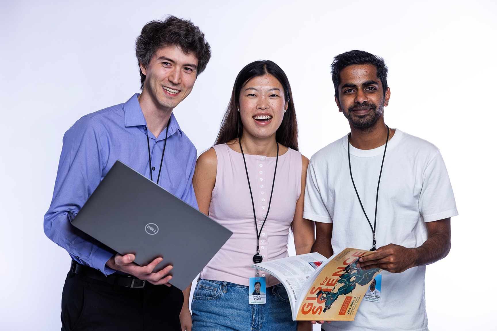 Three young adults stand together against a plain white background, smiling at the camera