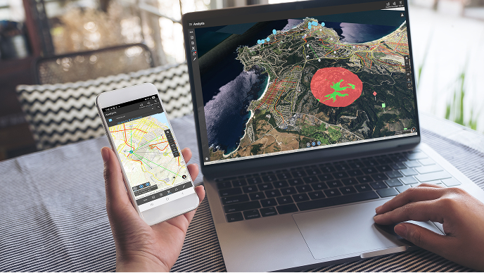 Mobile device being held next to a laptop with both showing a map that displays the results of analysis. 