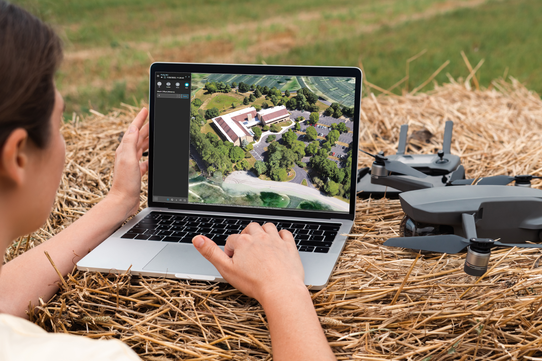 A student in a field next to a drone using a laptop with map image displayed.