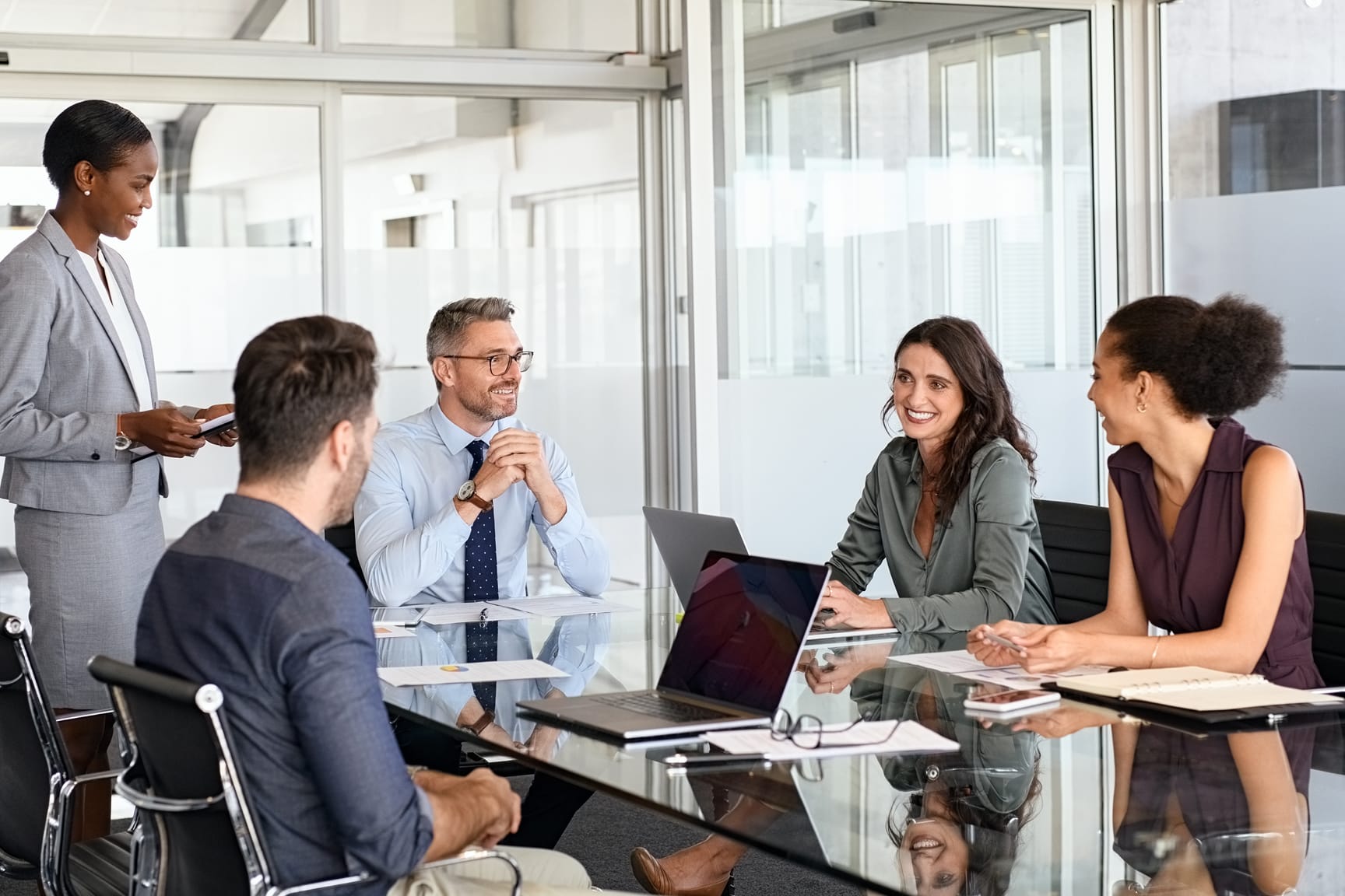 A group of professionals gathers around a glass conference table in a contemporary office setting.
