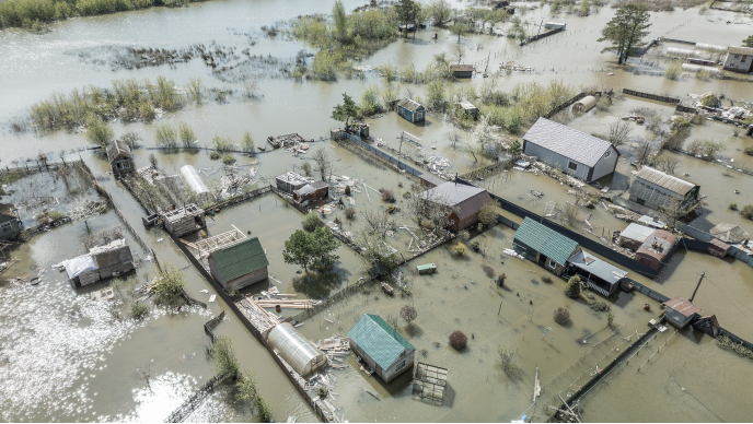 This image shows a rural neighborhood severely affected by flooding, with water covering yards, gardens, and partially submerging buildings.