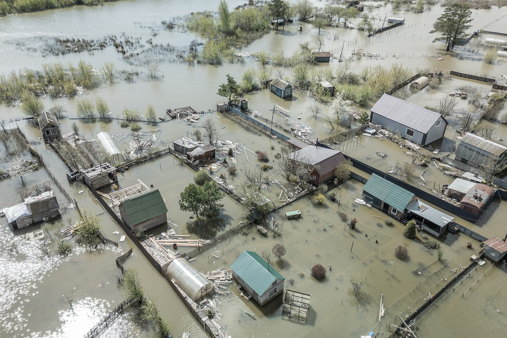 This image shows a rural neighborhood severely affected by flooding, with water covering homes, gardens, and roads