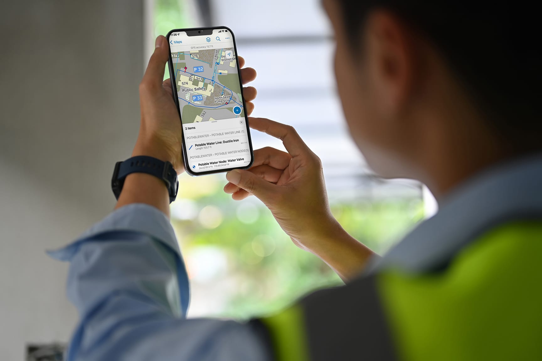 A man in a safety vest holds a smartphone displaying a map navigation application.