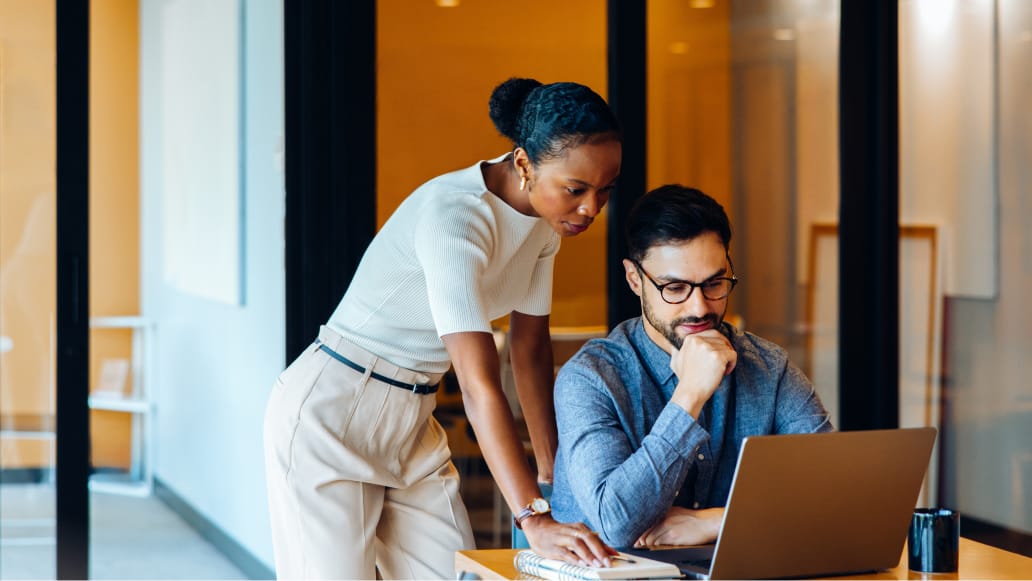 Two professionals are engaged in a collaborative discussion at a desk in a contemporary office setting. 