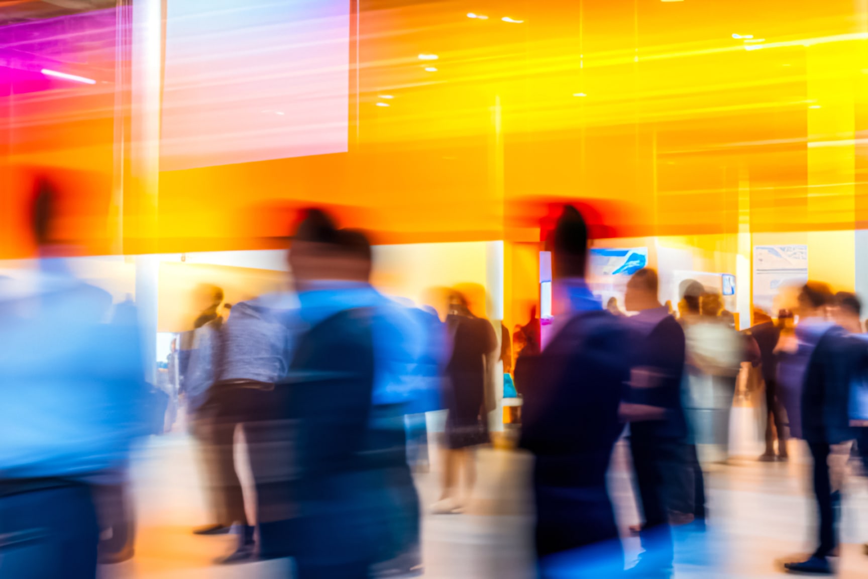 A group of people is seen moving through a brightly lit indoor space, captured with intentional motion blur. 