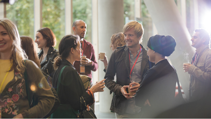 A group of adults gathers in a bright indoor space, engaging in conversation during a networking event