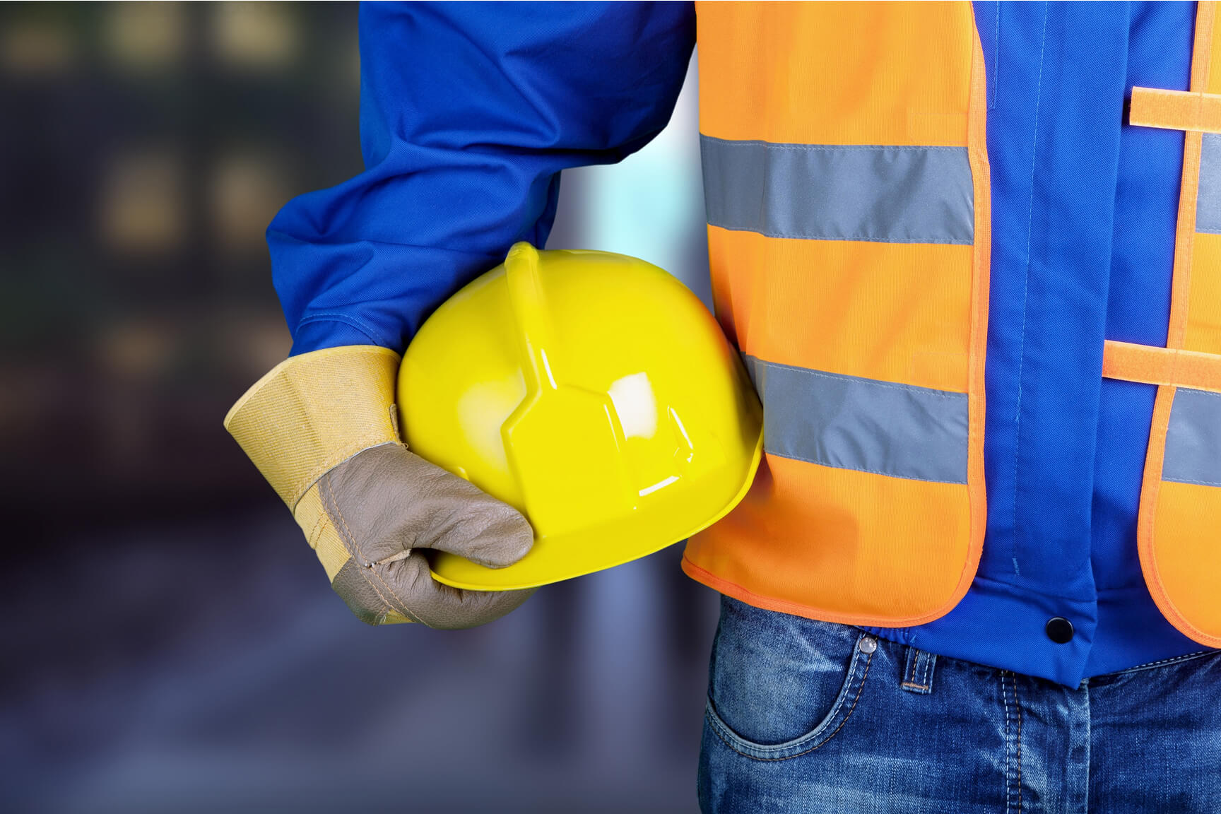 Close-up of a construction worker holding a bright yellow hard hat in one hand