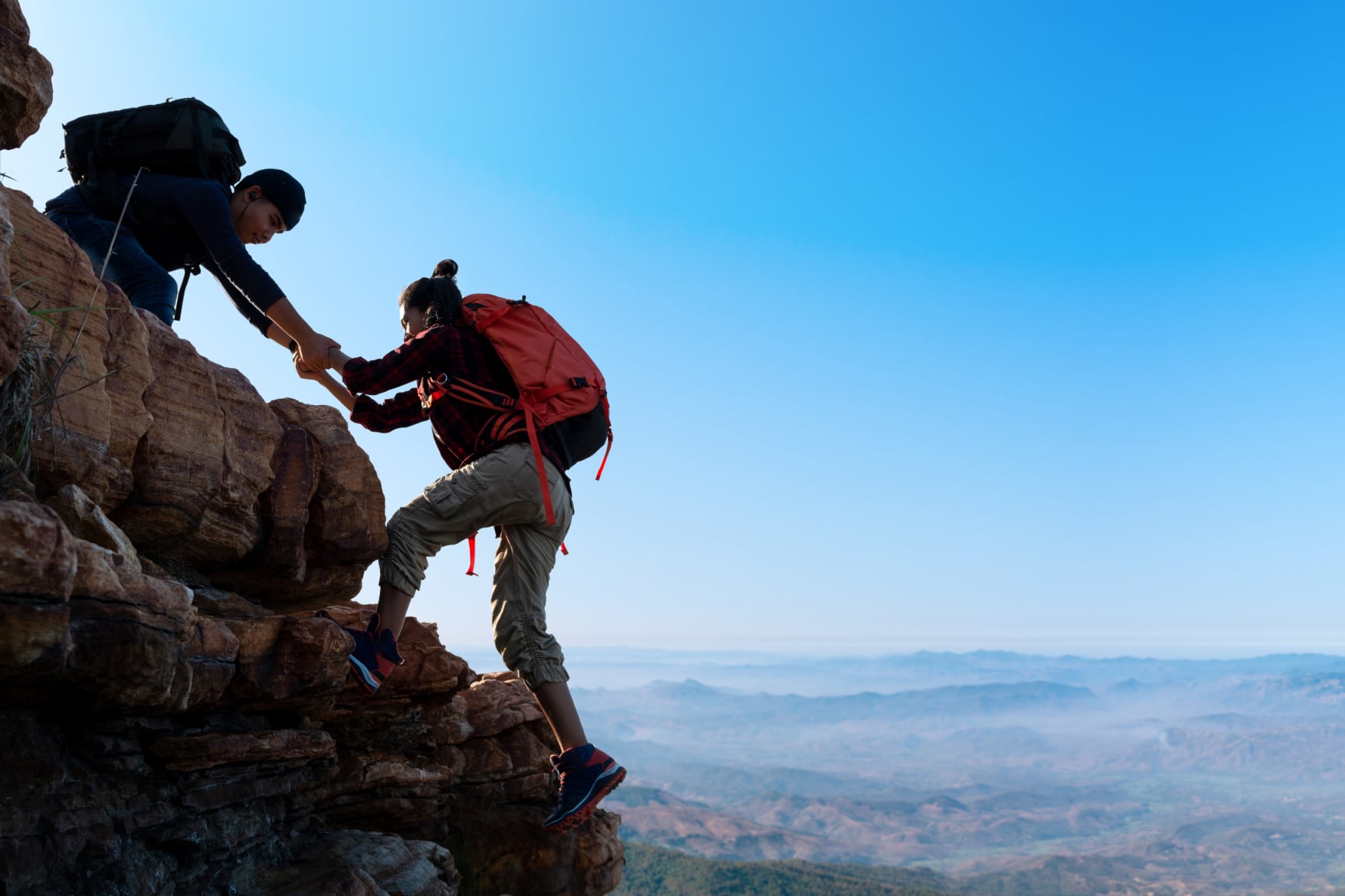 One hiker helps another onto a rocky summit