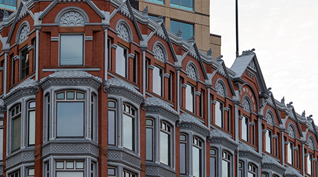 Rangée d’immeubles d’appartements à plusieurs étages de type ancien en brique rouge avec les fenêtres réfléchissant le ciel bleu