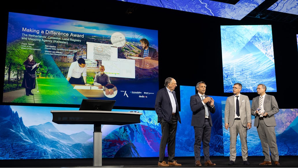 A group of four people wearing suits standing on a colorful stage presenting to an unseen audience