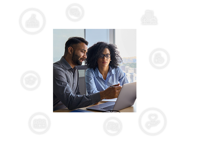 Two individuals in office setting working together on laptop with community engagement icons surrounding them