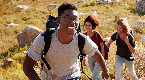 Three young adults smiling while backpacking through a field