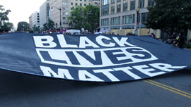 Large sign spread across a street reading “Black lives matter”