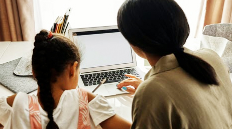 A caregiver and a child are seated with their backs turned to the camera looking at an open laptop screen
