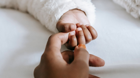 A baby’s hand in a long-sleeved white top is outstretched grabbing on to an adult hand