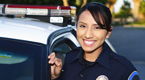 A smiling police officer standing outside the driver’s side door of a police car