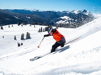 A skier going down a snowy hill with mountains in the background