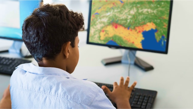A young child working on a desktop computer that is displaying a map