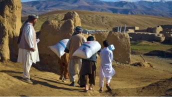 Five Afghanistan people carrying bags of food over their shoulders 