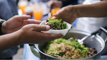 A person at a food kitchen being handed a bowl of salad by the person serving the food