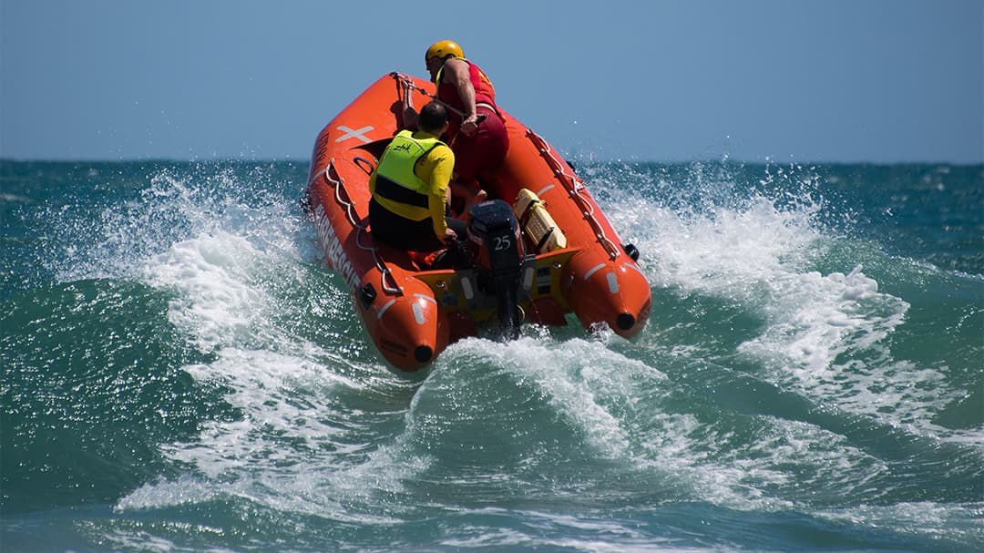 A rescue team navigates an orange inflatable boat through rough ocean waves.