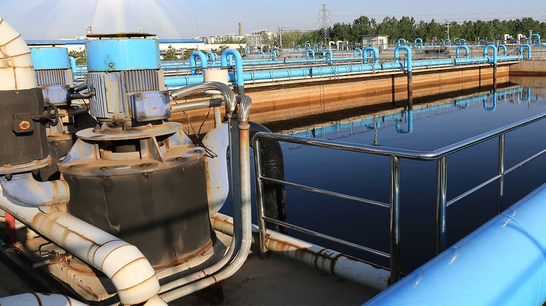 An outdoor industrial water treatment facility featuring large tanks and piping systems. 