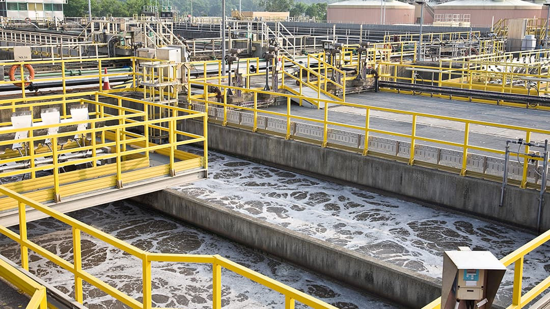 An outdoor wastewater treatment plant featuring large tanks and yellow railings. 