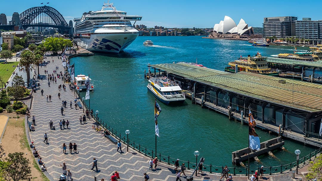 A large cruise ship is docked near the iconic Sydney Opera House in Sydney Harbour. 