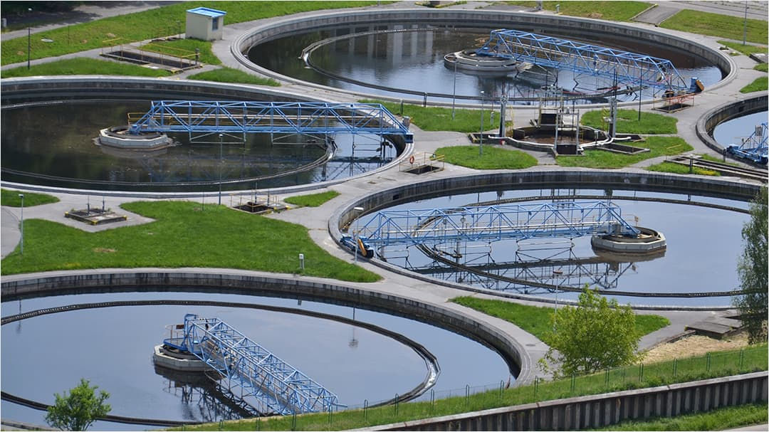 A large wastewater treatment facility featuring multiple circular sedimentation tanks surrounded by green grass.