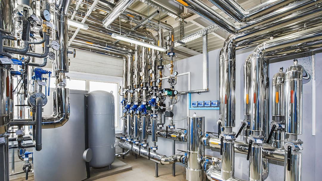 A complex network of stainless steel pipes and tanks in an industrial setting. 