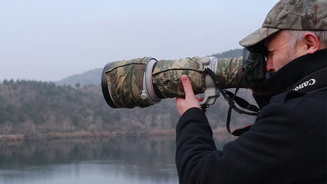 A photographer is seen holding a camera equipped with a camouflage-patterned telephoto lens.