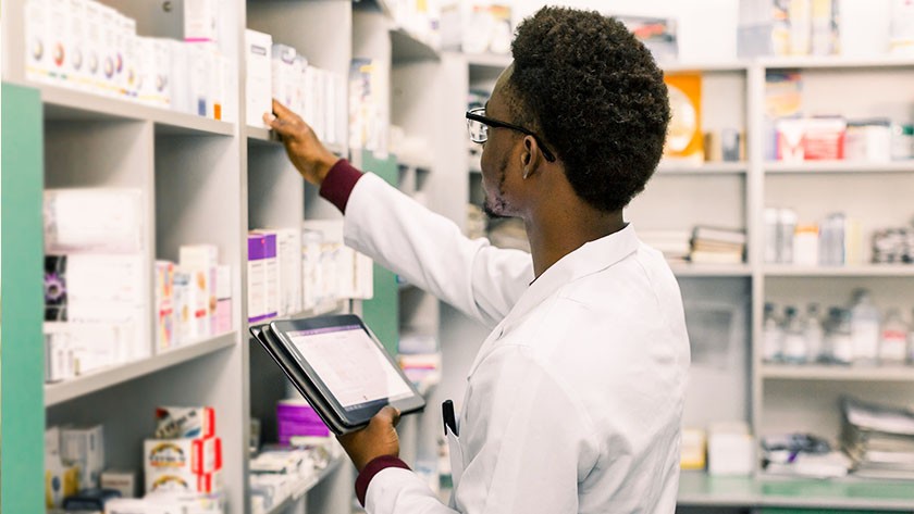 Pharmacist checking medication stocks while consulting a tablet